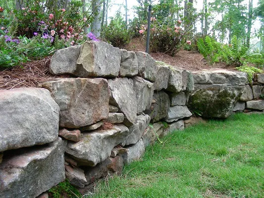 Natural boulder retaining wall construction for hillside stability and erosion control featuring boulder placement sequencing for slope retention and natural aesthetics in Post Falls, Coeur d'Alene, and North Idaho